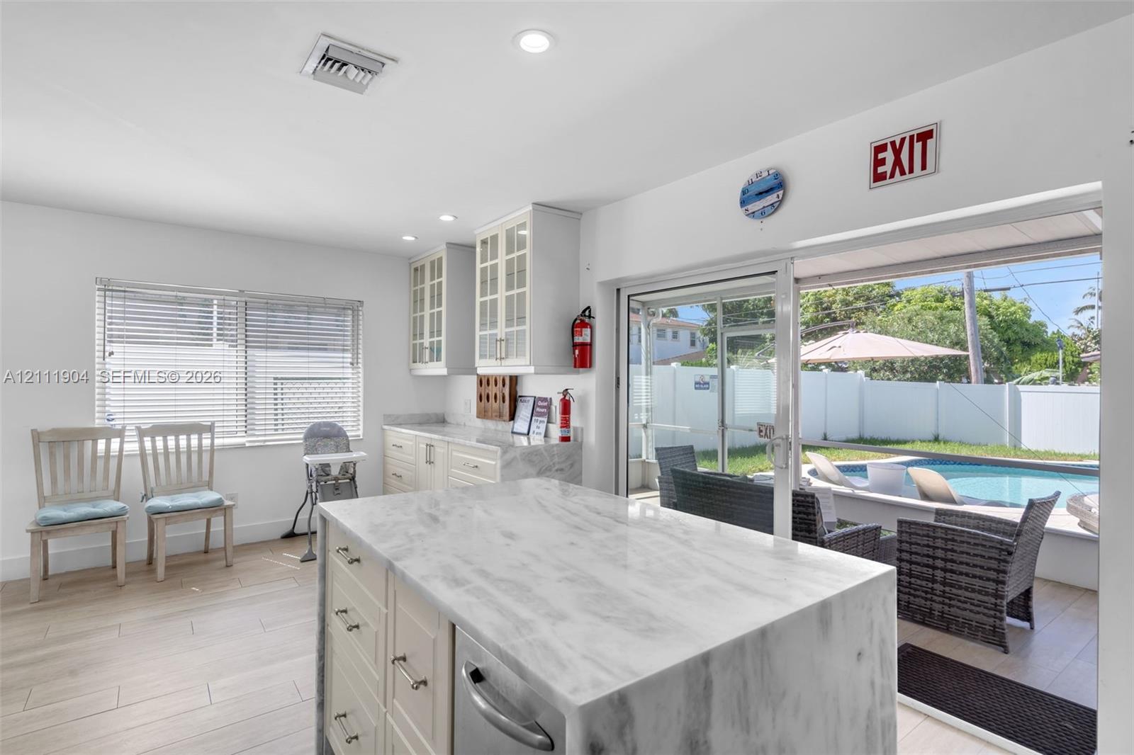 Kitchen featuring a stone-topped waterfall island, custom cabinetry with glass-front uppers, wood-finish flooring, recessed lighting, and a sliding glass door providing external access to the pool area