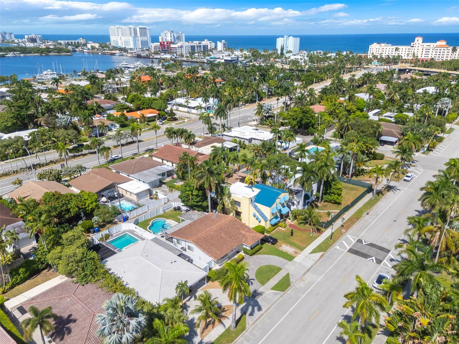 Aerial perspective of coastal residential property featuring mature palm landscaping, paved driveway, and proximity to the waterfront