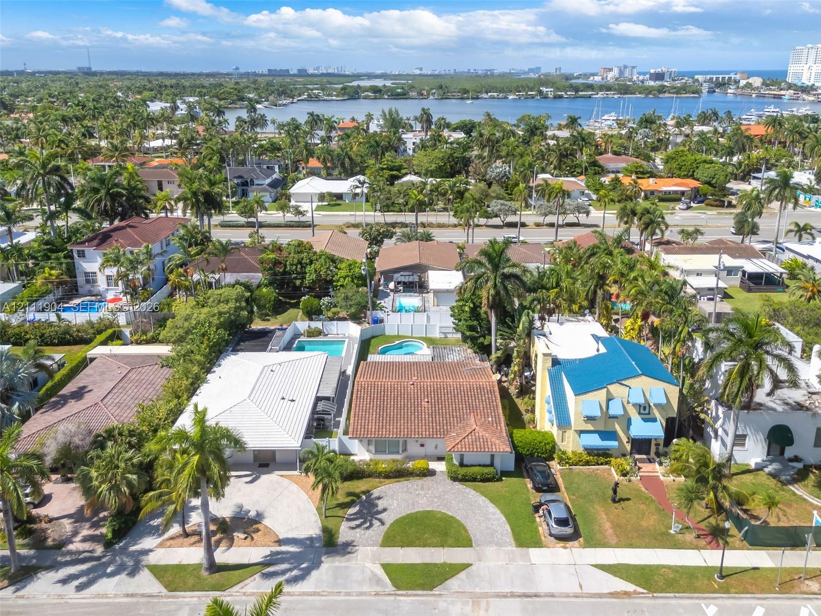 Residential lot featuring a circular paved driveway, mature palm trees, and an in-ground swimming pool enclosed by privacy fencing