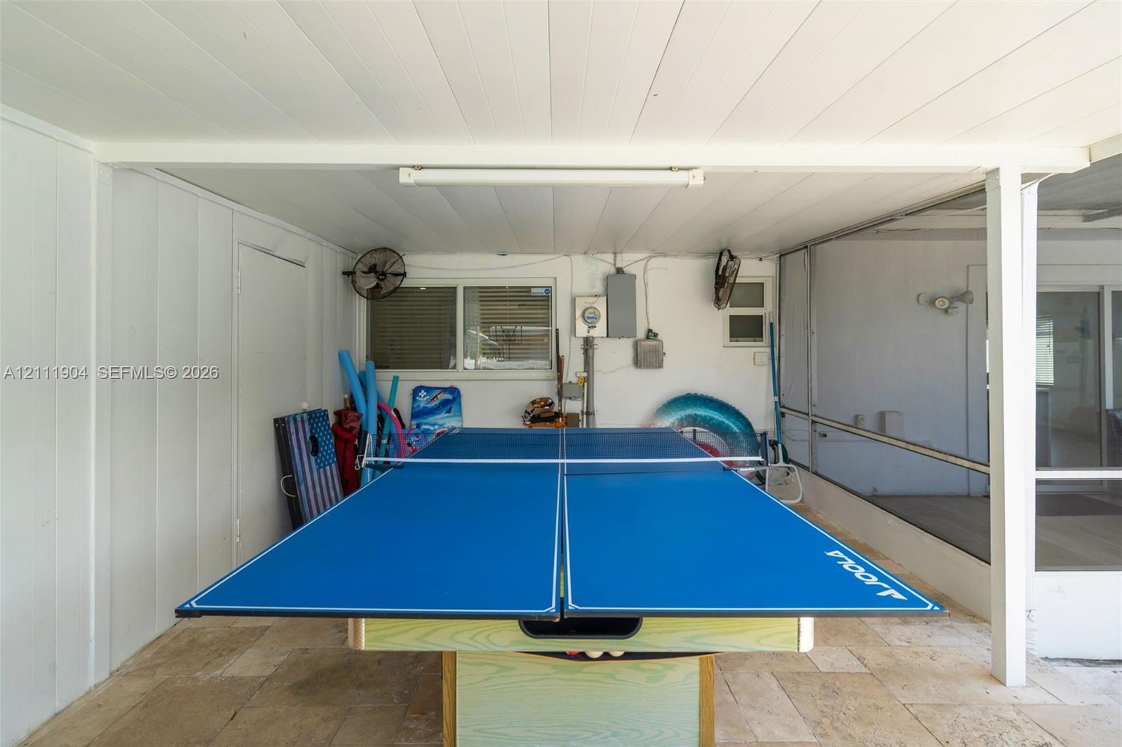 Covered patio featuring stone-tile flooring, screen enclosure, ceiling-mounted fans, and white vertical panel siding