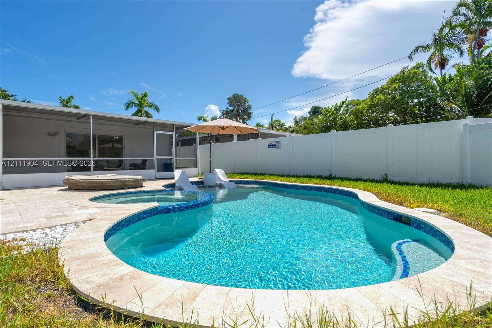 Free-form in-ground swimming pool with an integrated spa, stone-paver decking, screened-in patio, and vinyl privacy fencing