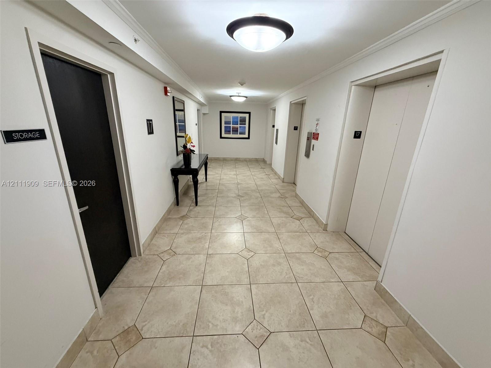 Hallway featuring neutral tile flooring with diamond-patterned inlay, ceiling-mounted dome lighting, and multiple elevator access points