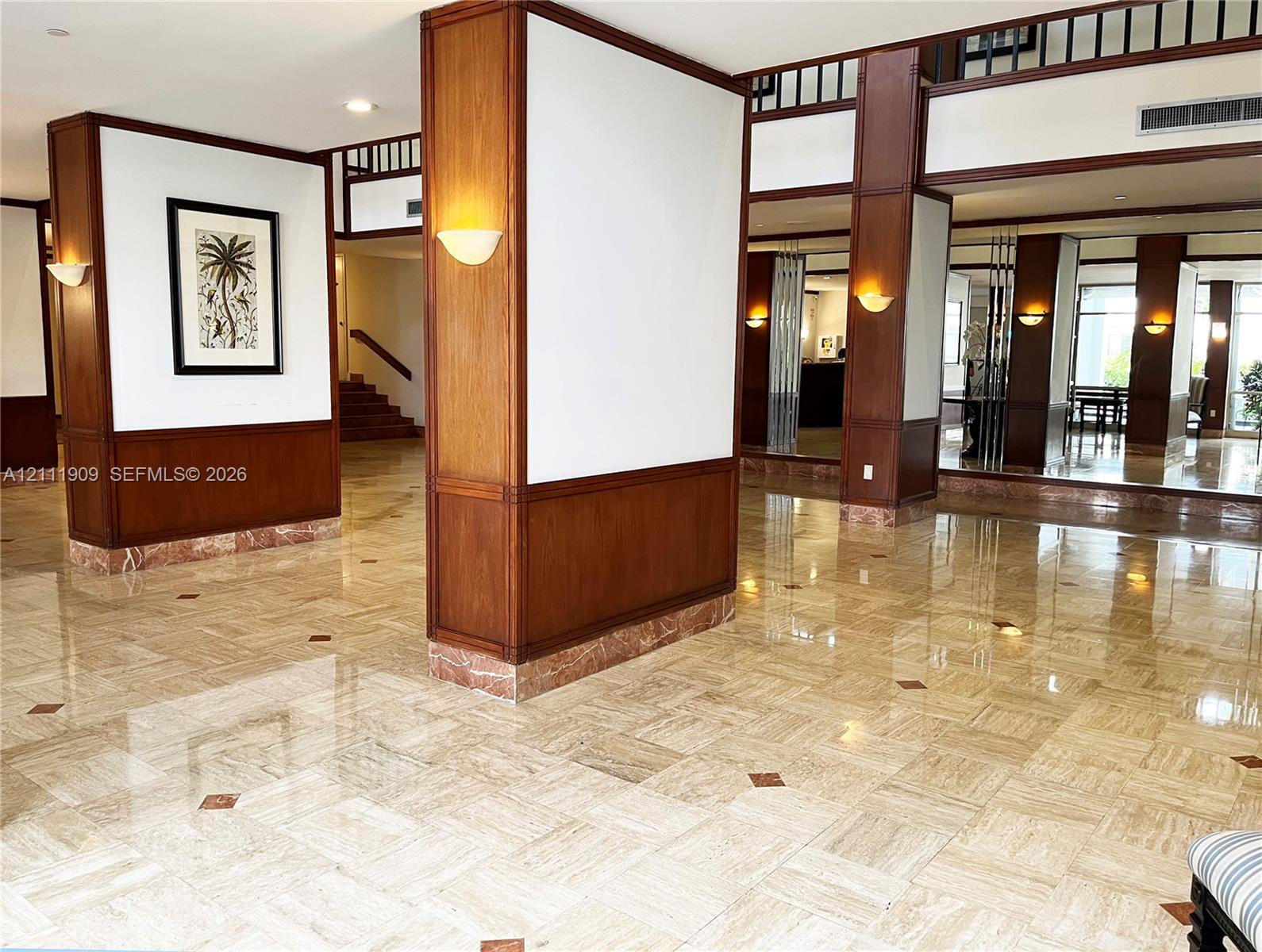 Polished stone tile flooring with decorative stone inlays, wood-paneled support columns, wall-mounted sconce lighting, and a mezzanine-level wood railing