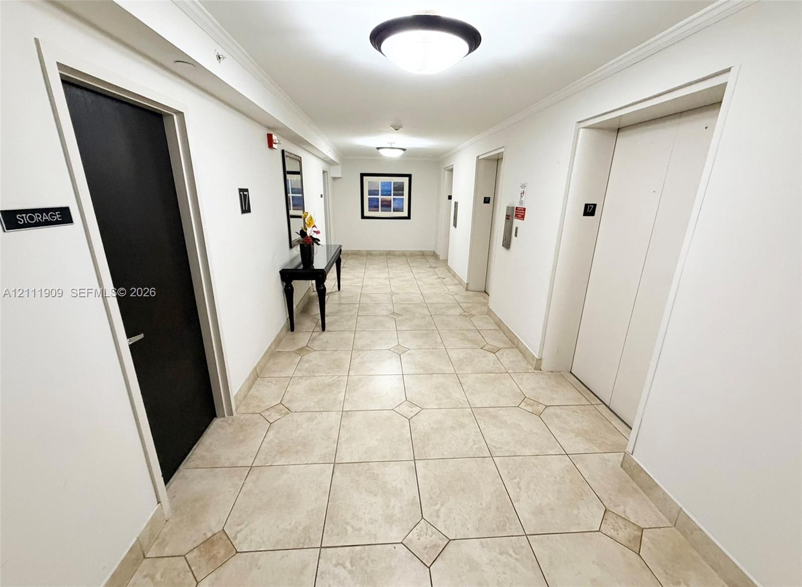 Hallway featuring large-format tile flooring with diamond-pattern accents, recessed ceiling lighting, and dual elevator access