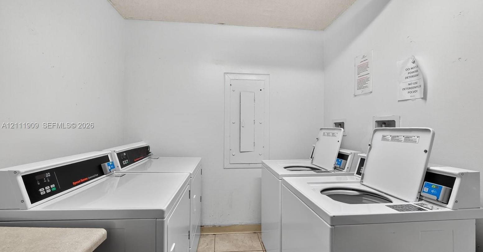 Laundry room featuring multiple high-capacity commercial-grade top-load washers and dryers and neutral tile flooring