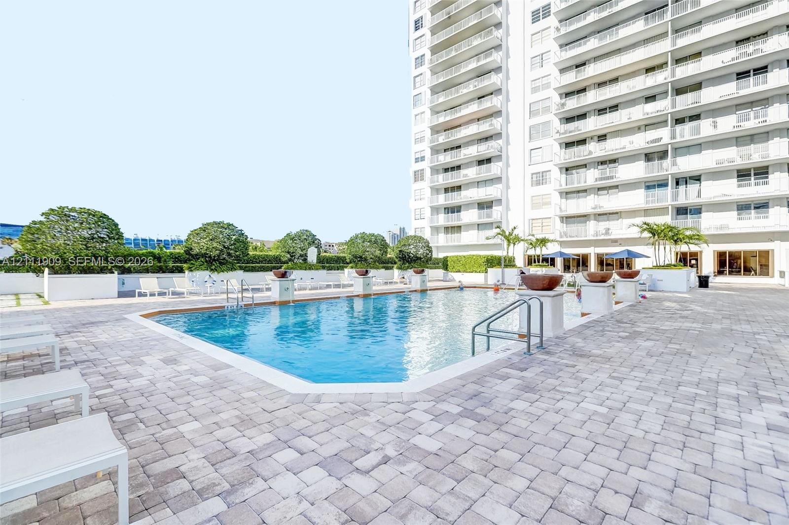Swimming pool with metallic handrails, surrounding paver decking, and decorative stone planters