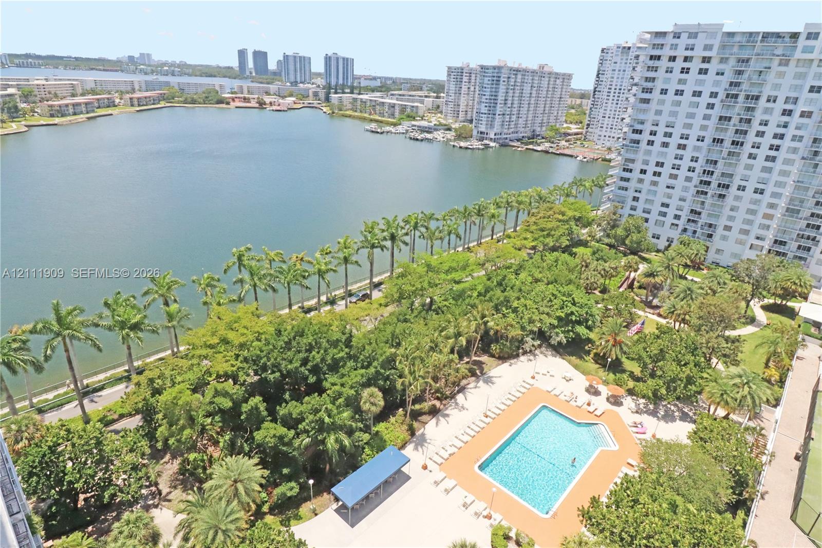 Elevated aerial perspective featuring a waterfront location, expansive lake, swimming pool with deck, mature landscaping, and palm trees