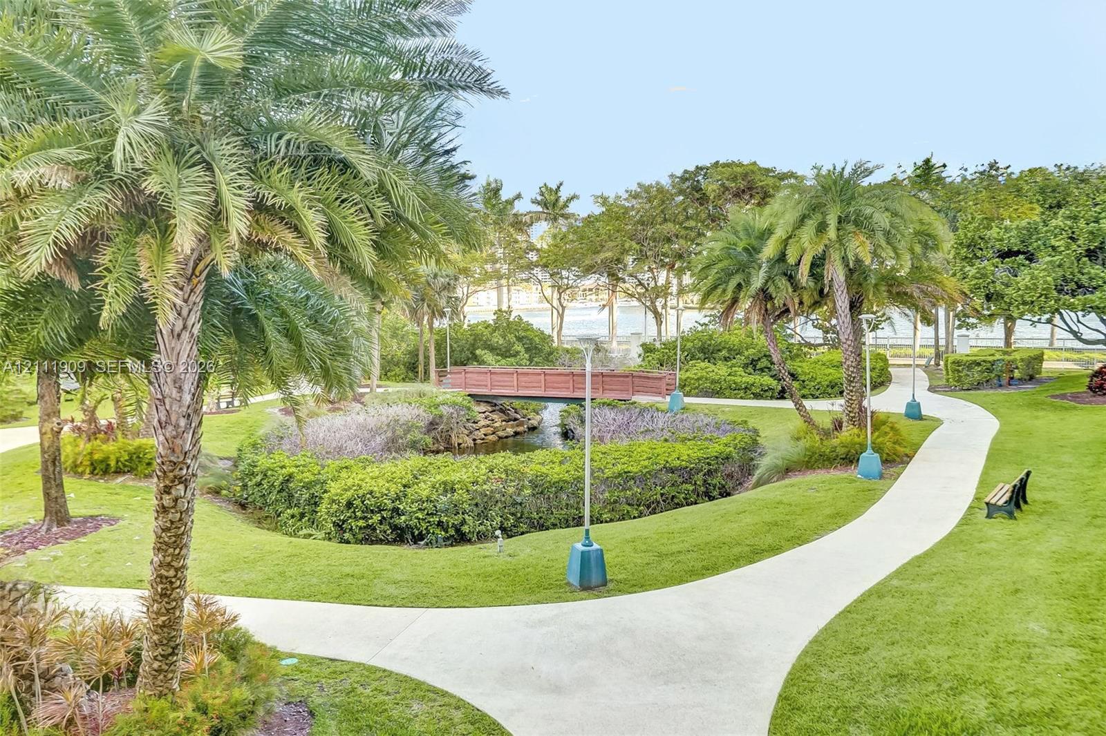 Landscaped grounds featuring palm trees, a concrete pathway, a decorative wooden bridge, and a water feature