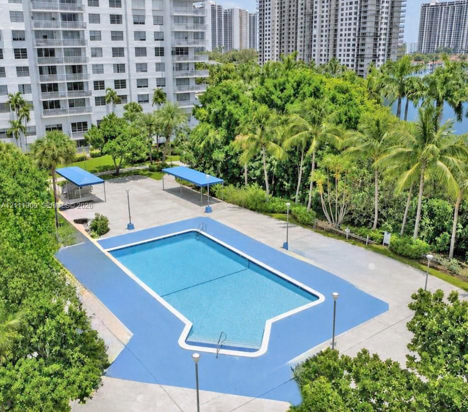 Outdoor swimming pool featuring a concrete deck, shaded seating areas, pedestal lighting, and lush perimeter landscaping