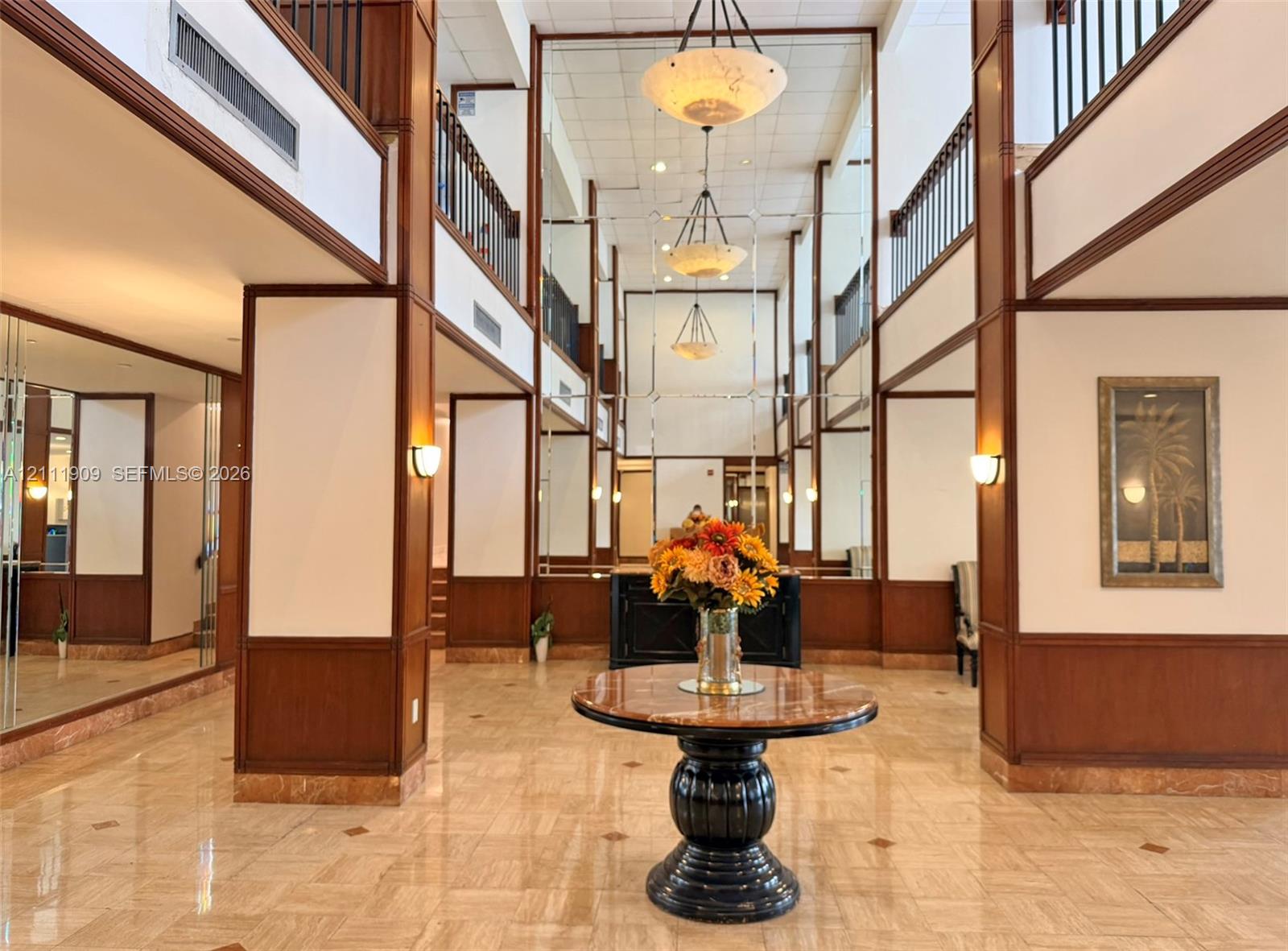 Multi-story lobby featuring stone flooring, full-height mirrored wall panels, wood-trimmed architectural columns, tiered pendant lighting, and metal balcony railings