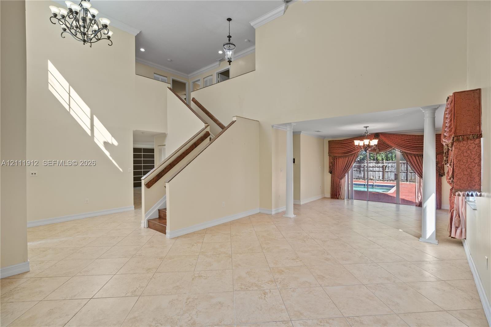 Grand foyer featuring a double-height ceiling, staircase with a wood handrail, decorative chandeliers, tile flooring, and column supports