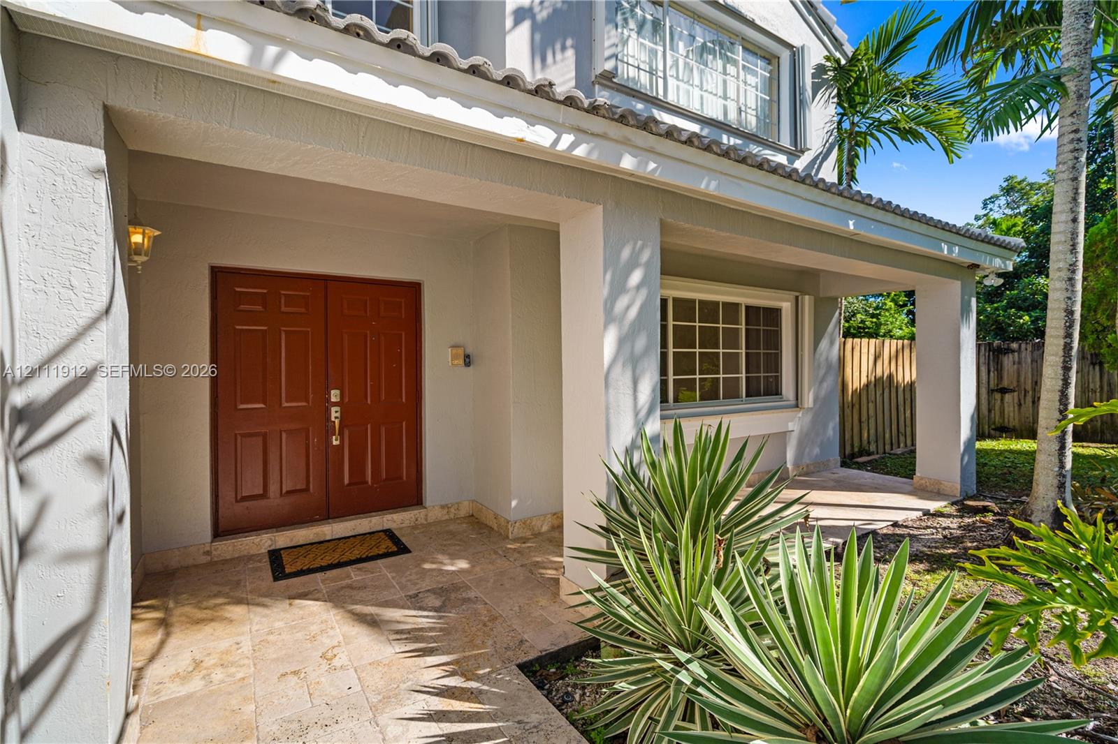 Covered front porch featuring natural stone flooring, double entry doors, stucco exterior walls, and tiled roof architecture