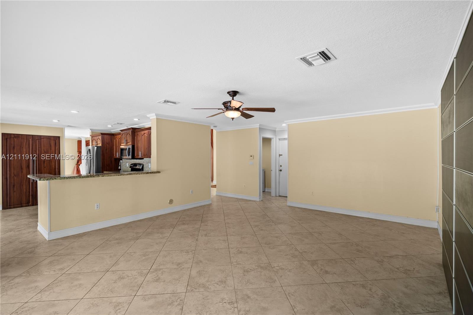Interior space featuring tile flooring, ceiling-mounted fan, stone-surfaced kitchen breakfast bar, and dark wood-finish cabinetry