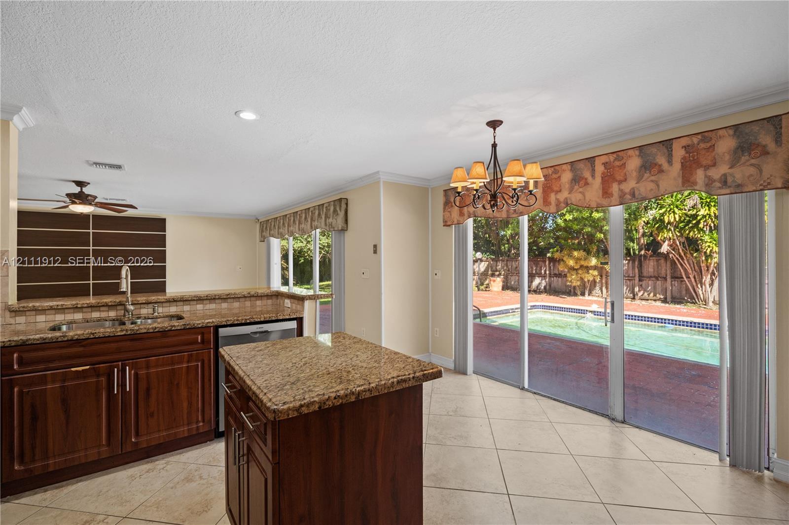 Kitchen featuring wood cabinetry, stone-surface countertops, central island, tile flooring, and sliding glass doors leading to an outdoor pool area