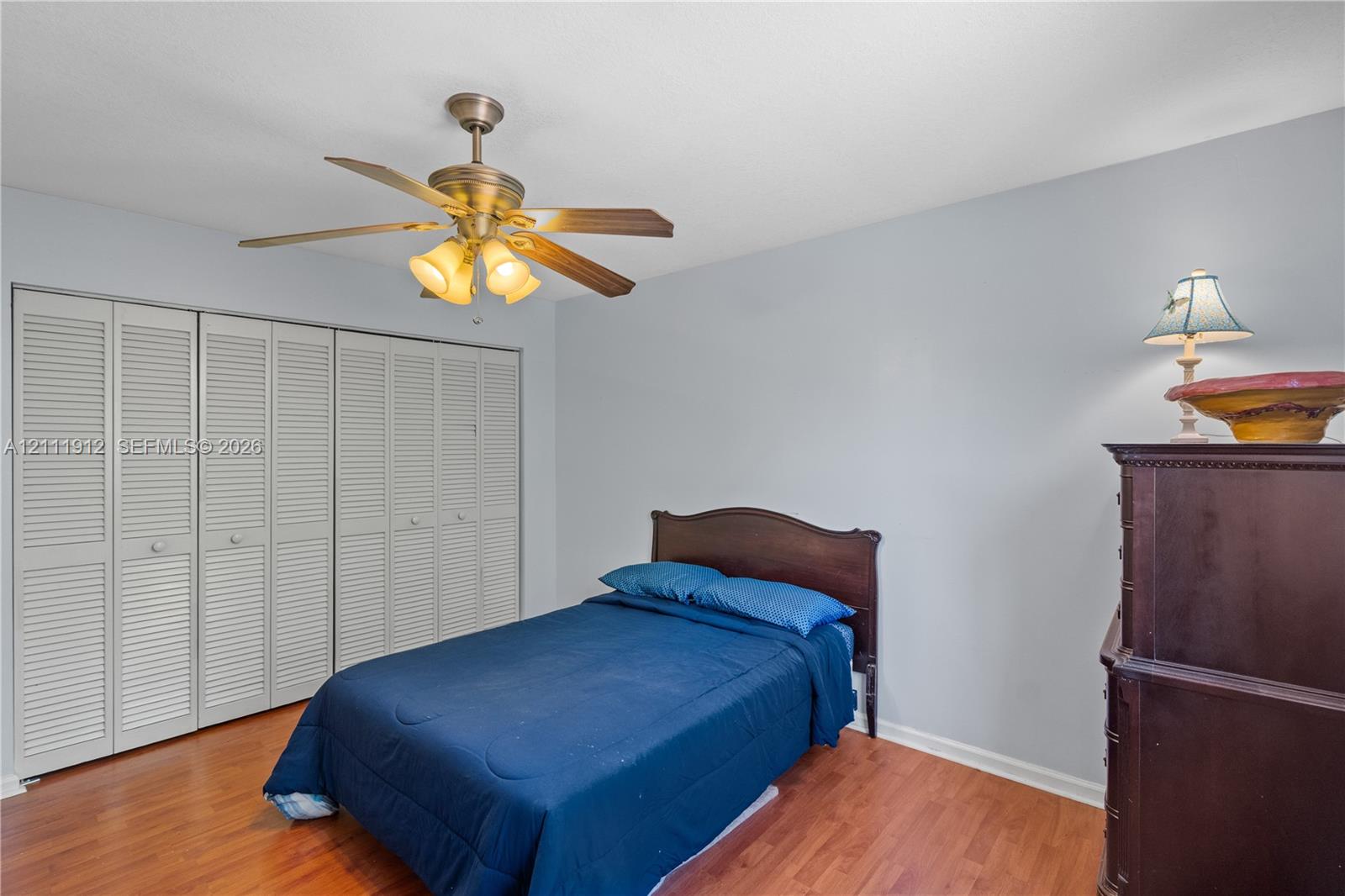 Room featuring wood-finish flooring, floor-to-ceiling louvered closet doors, and a multi-light ceiling fan
