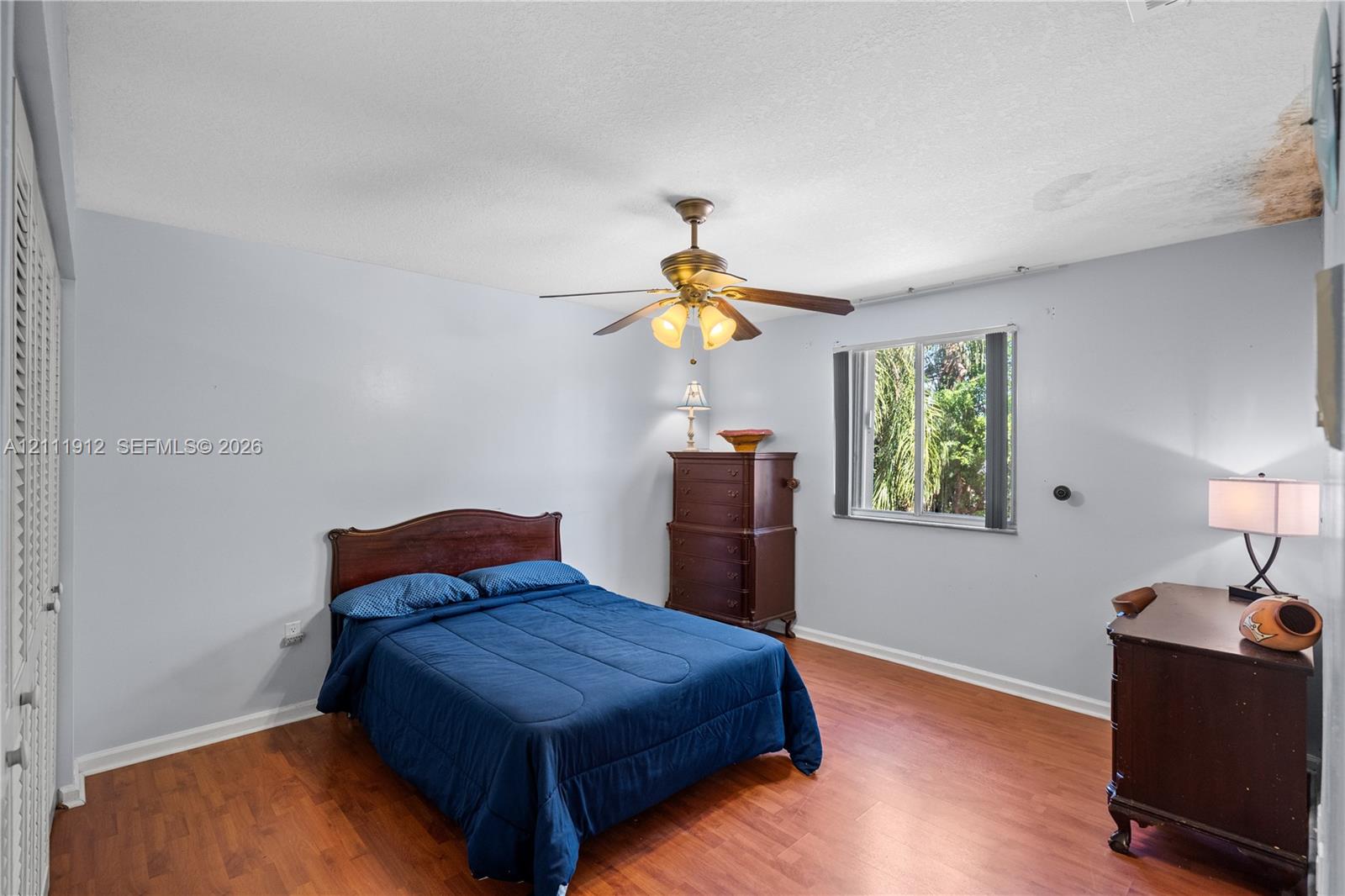 Room featuring wood-finish flooring, a ceiling fan with integrated lighting, and a window with exterior greenery