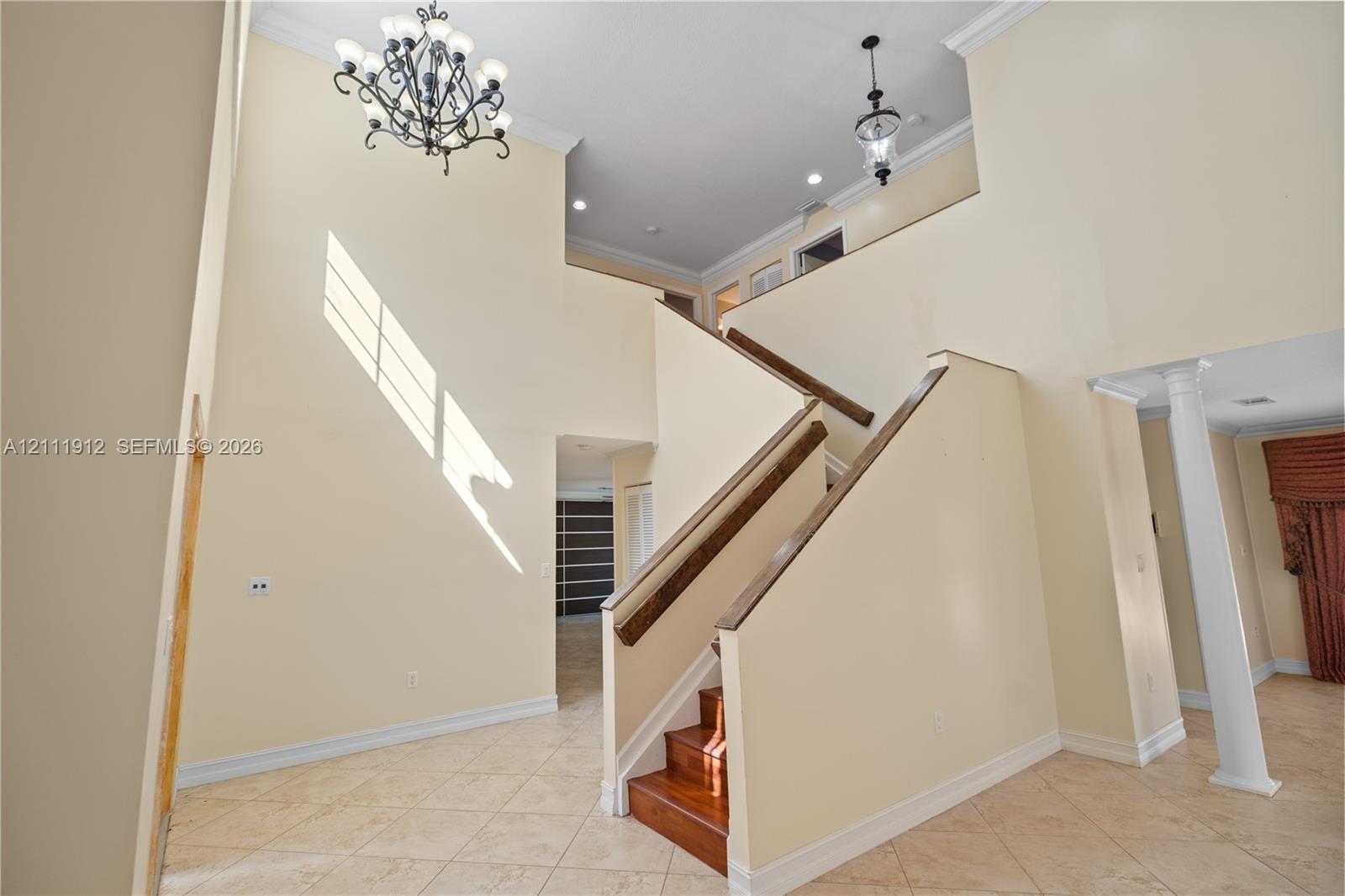 Two-story foyer featuring high ceilings, a decorative wrought-iron chandelier, tile flooring, a prominent staircase with wood treads and handrails, and a structural column