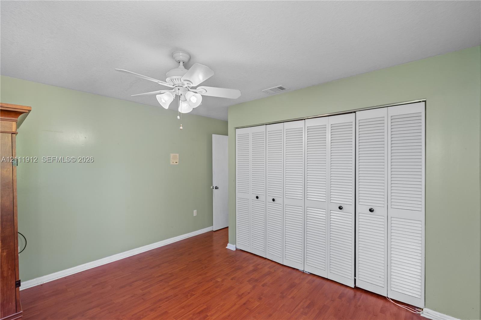 Wood-finish flooring, white louvered bifold closet doors, and a ceiling fan with integrated multi-light fixture