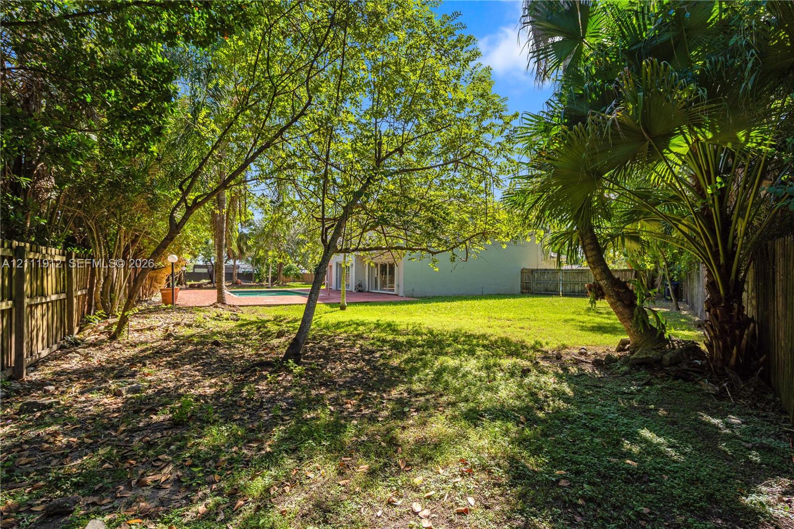 Expansive backyard featuring mature trees, a manicured lawn, a swimming pool, a paved patio area, and wood fencing