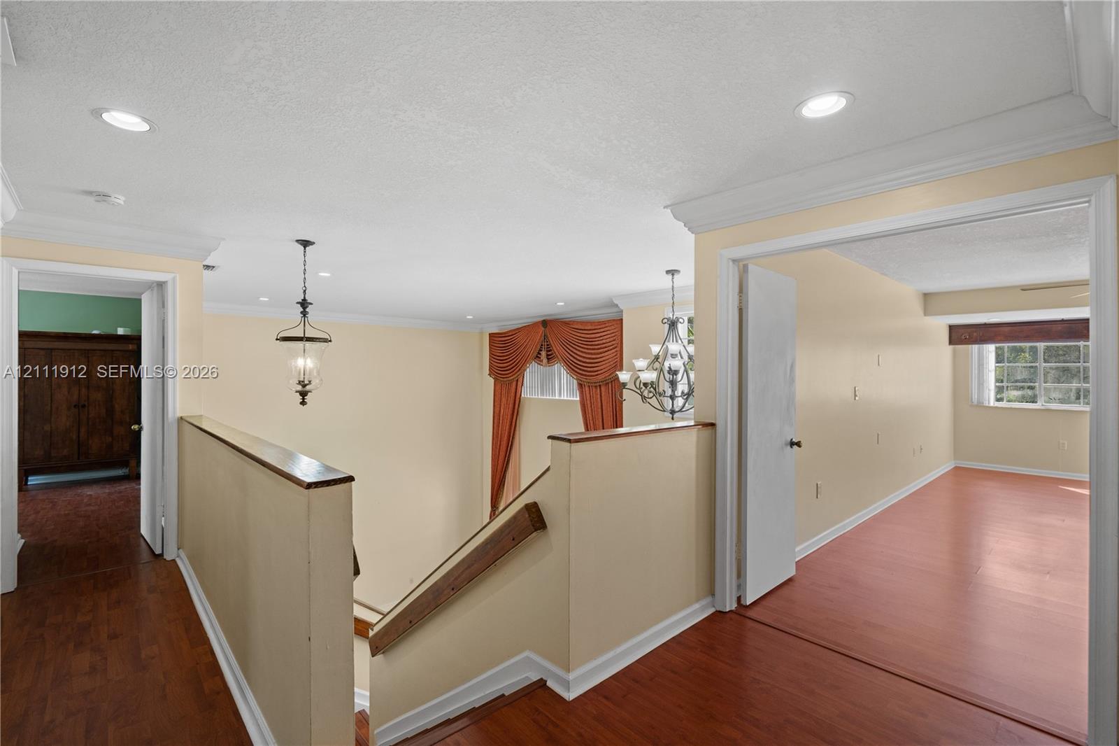 Interior landing featuring wood-finish flooring, recessed lighting, crown molding, a decorative metal chandelier, and a wood-capped half wall