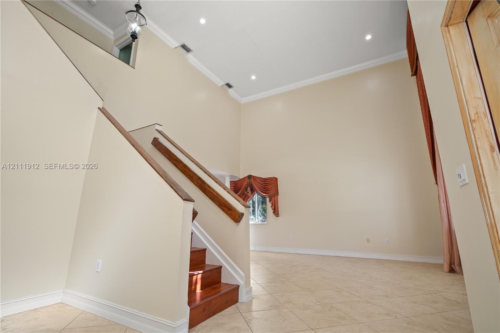 Double-height ceiling, staircase with wood handrail, recessed lighting, and tile flooring