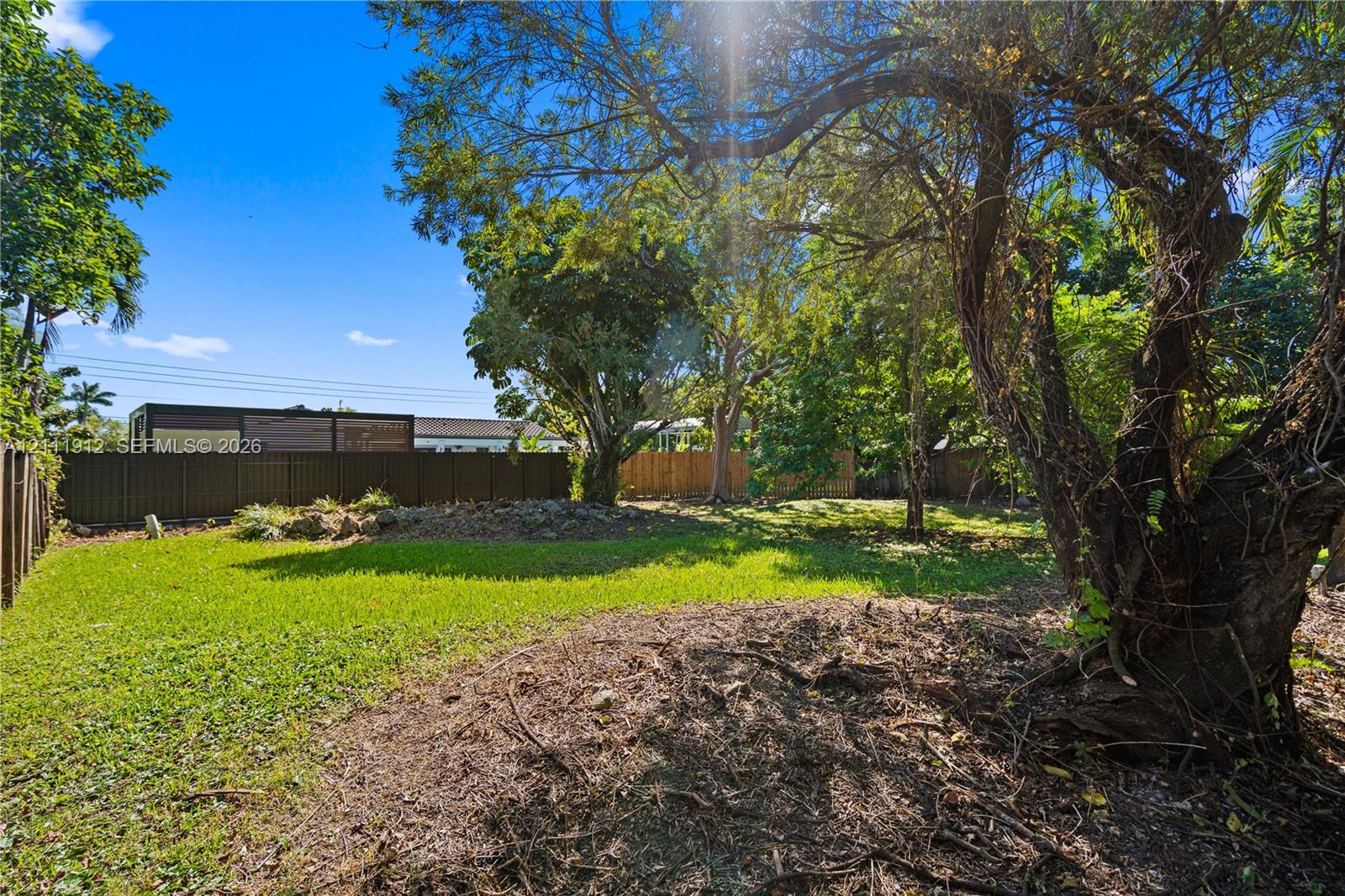 Backyard featuring a manicured lawn, mature trees, and a full-perimeter privacy fence