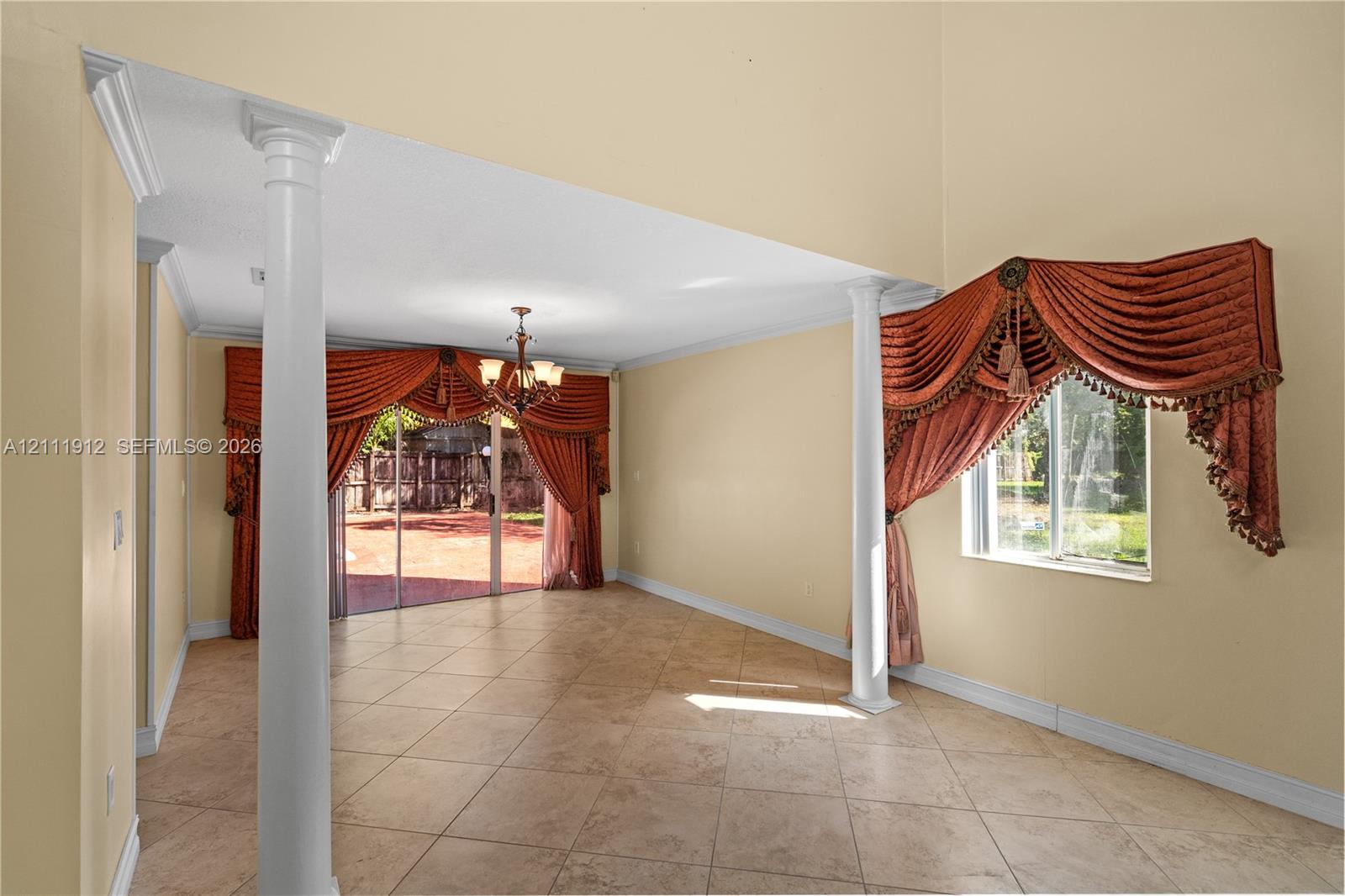 Interior space featuring high ceilings, large-format tile flooring, decorative architectural columns, and sliding glass doors