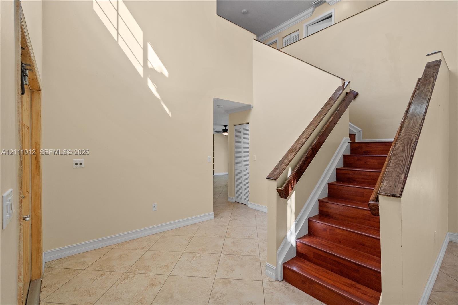 High-ceiling foyer featuring tile flooring, a staircase with wood-finish treads, and a custom wood handrail