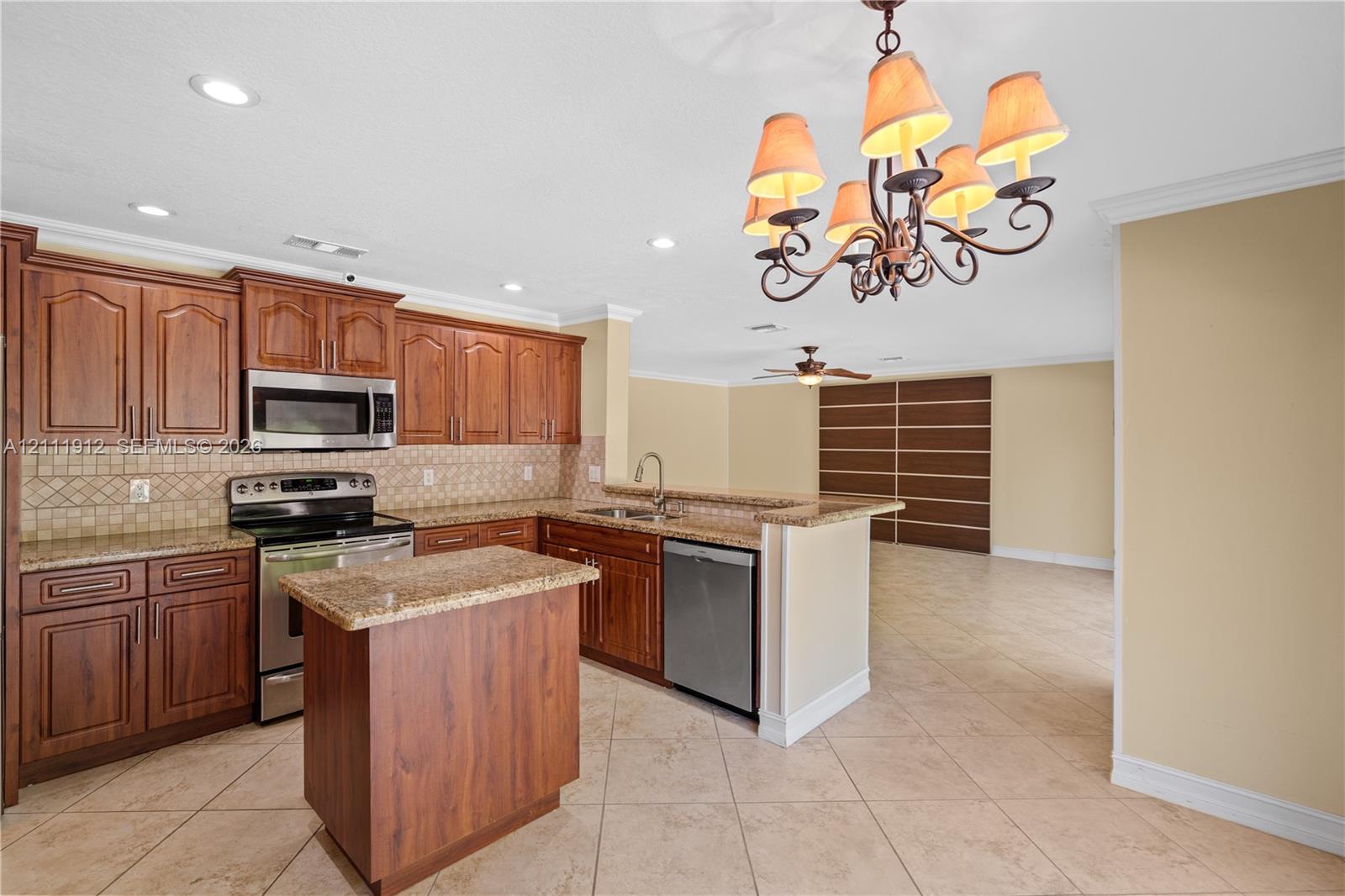 Kitchen featuring wood cabinetry, stone-finish countertops, stainless steel appliances, a center island, and a multi-arm chandelier