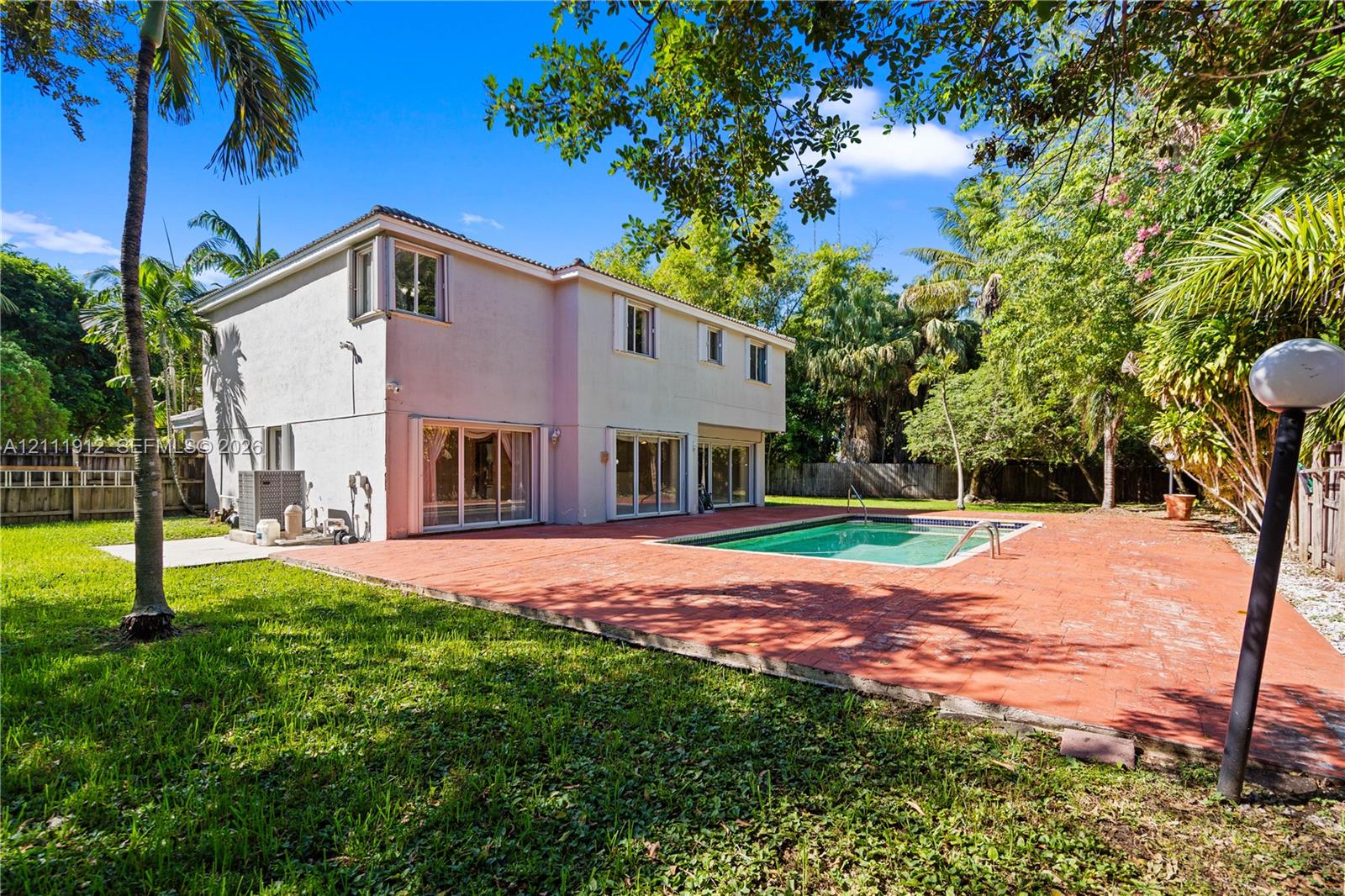 Two-story exterior featuring a stucco facade, in-ground swimming pool, expansive paved patio, and mature landscaping