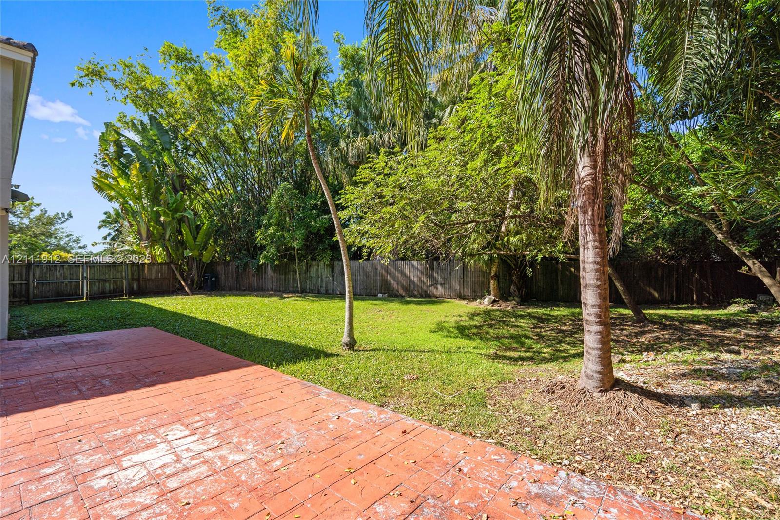 Rear patio featuring stamped concrete, expansive lawn, perimeter wood fencing, and mature palms