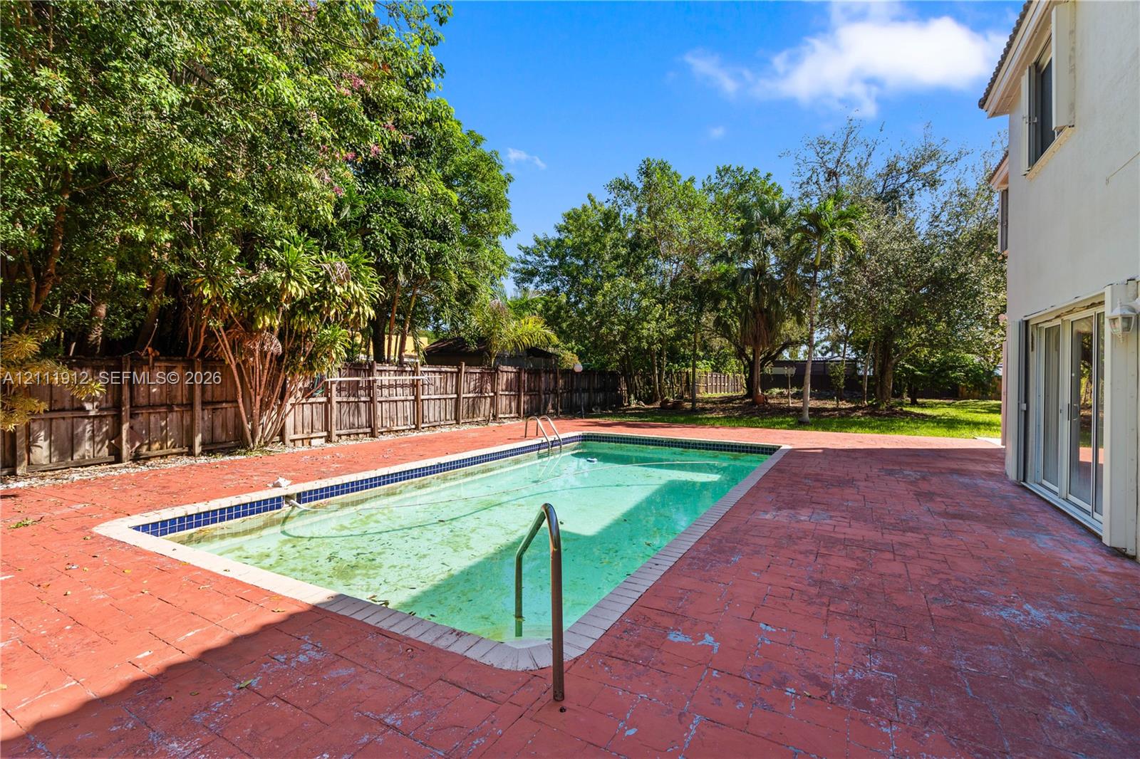 In-ground swimming pool featuring a tiled waterline, surrounded by an expansive paved patio and a wood-slat privacy fence