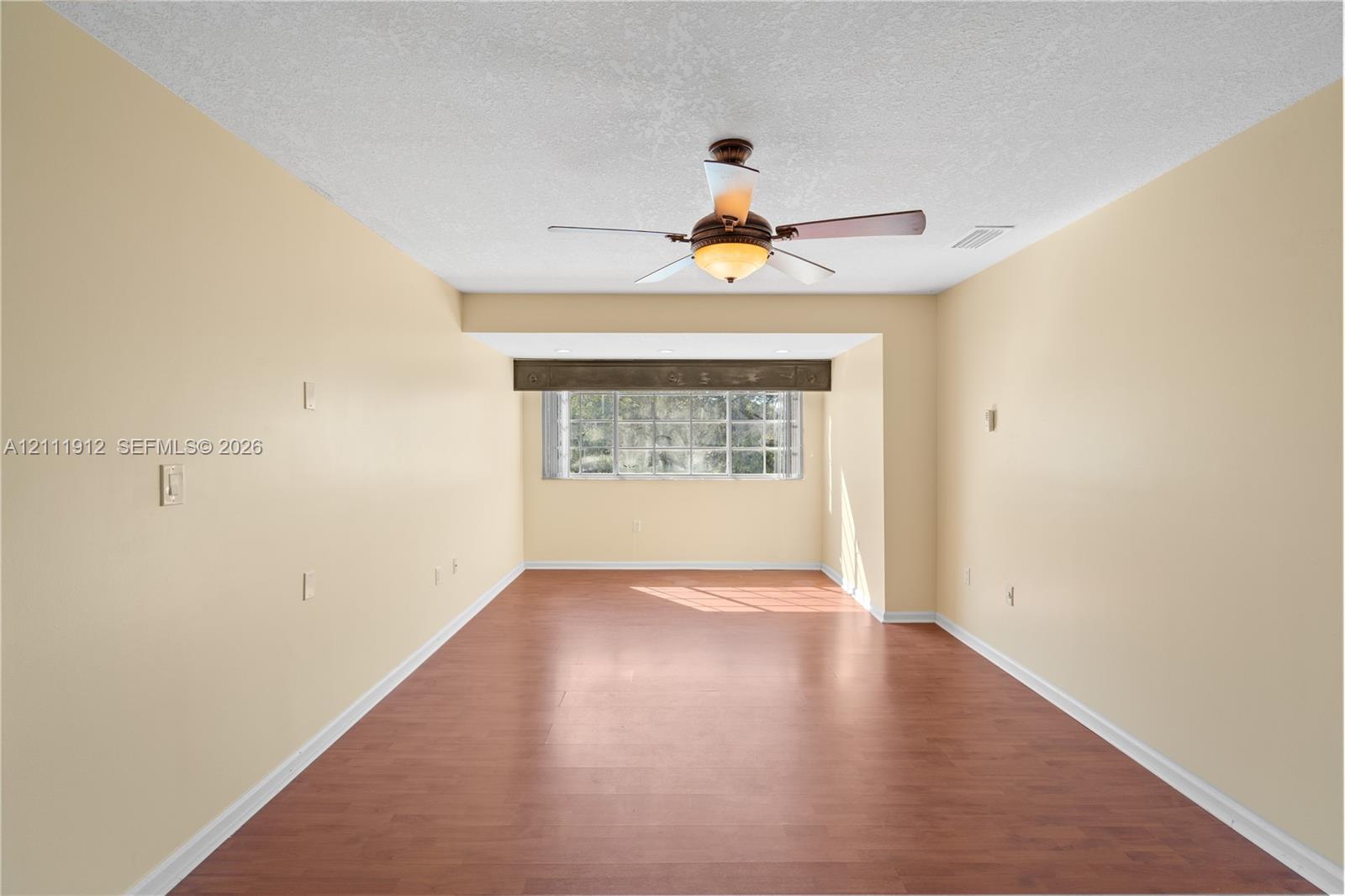 Interior room featuring wood-finish flooring, a multi-pane window with a decorative valance, and a ceiling-mounted light fixture with integrated fan blades