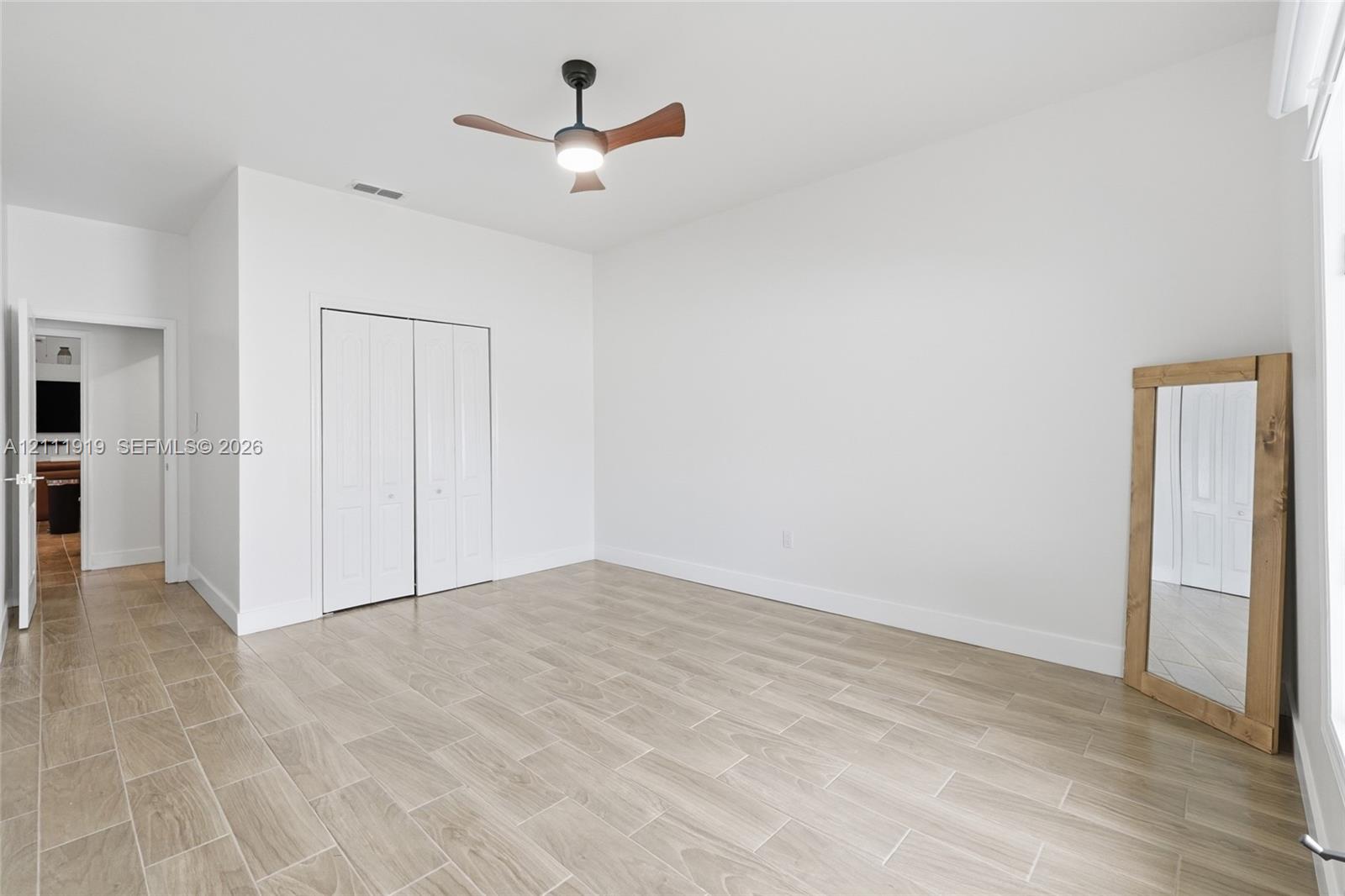 Neutral interior space featuring wood-finish tile flooring, recessed LED ceiling fan with integrated lighting, and white bi-fold closet doors