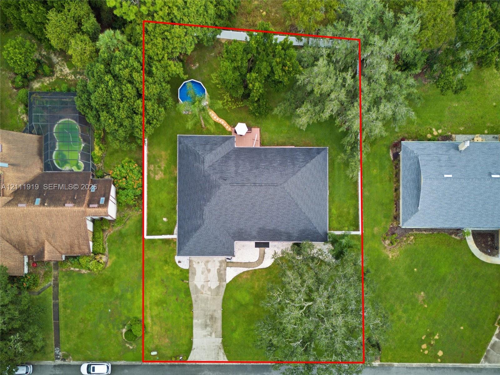 Aerial perspective of a property featuring a multi-hipped roof, concrete driveway, rear deck, and mature landscaping