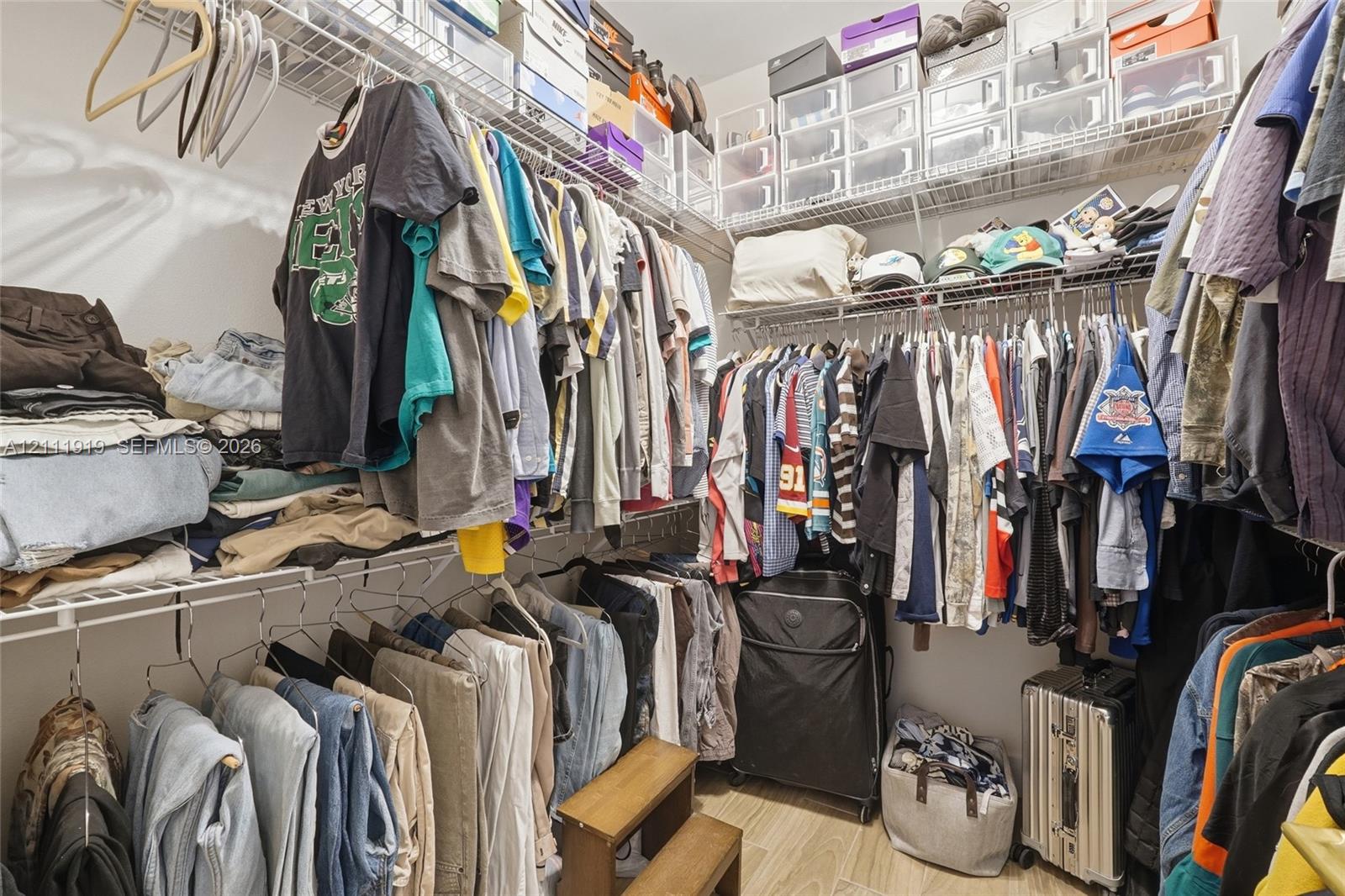 Walk-in storage space featuring multi-tiered white wire shelving systems and wood-finish flooring