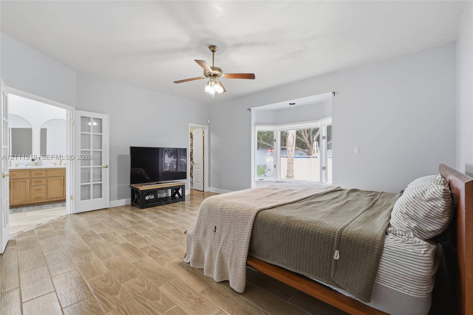 Room featuring wood-finish tile flooring, a bay window, a ceiling fan with integrated lighting, and French doors