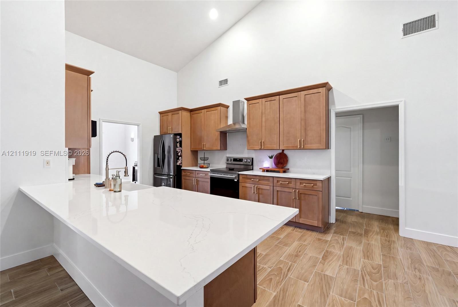 Kitchen featuring vaulted ceilings, wood-finish flooring, quartz countertops, shaker-style wood cabinetry, and stainless steel appliances