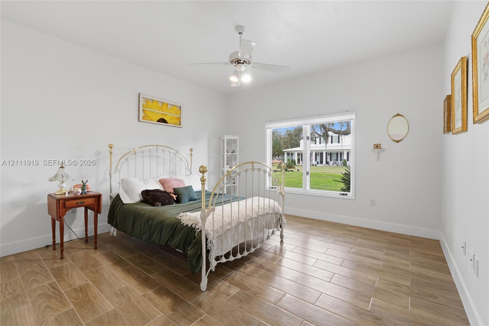 Neutral-toned room featuring wood-finish flooring, a large window, and a white ceiling fan with integrated lighting