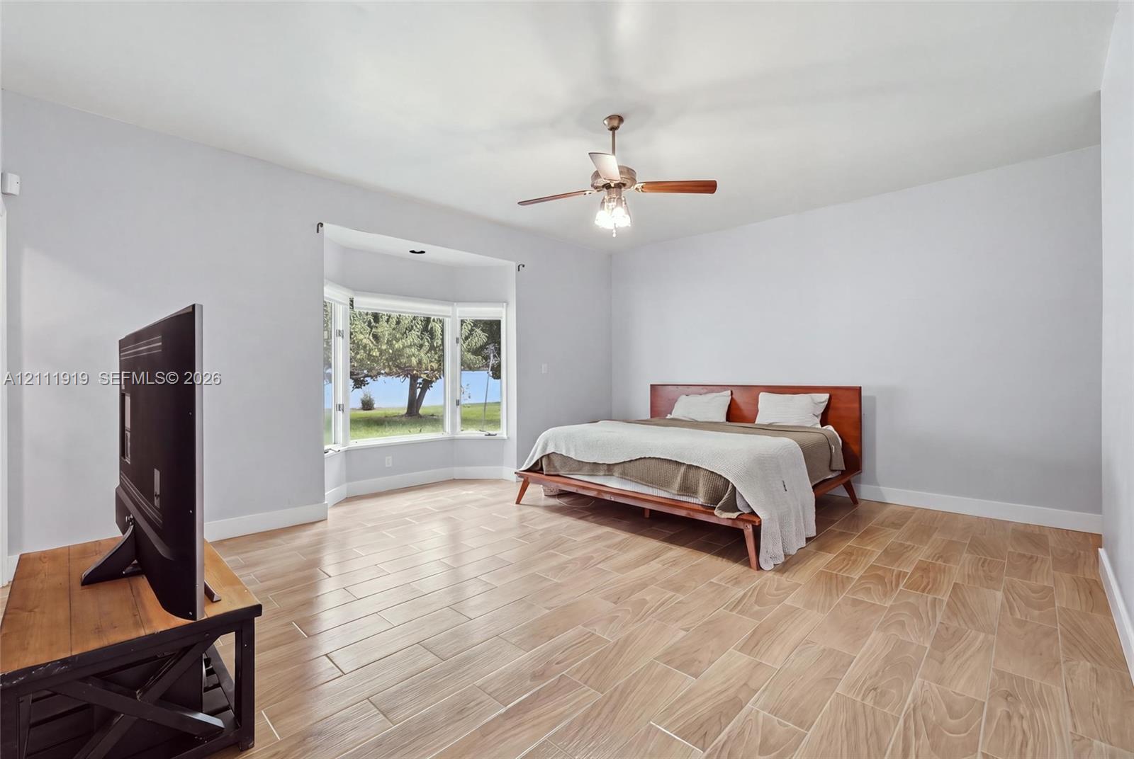 Spacious room featuring wood-finish flooring, a prominent bay window, and a ceiling-mounted light fixture with a central fan