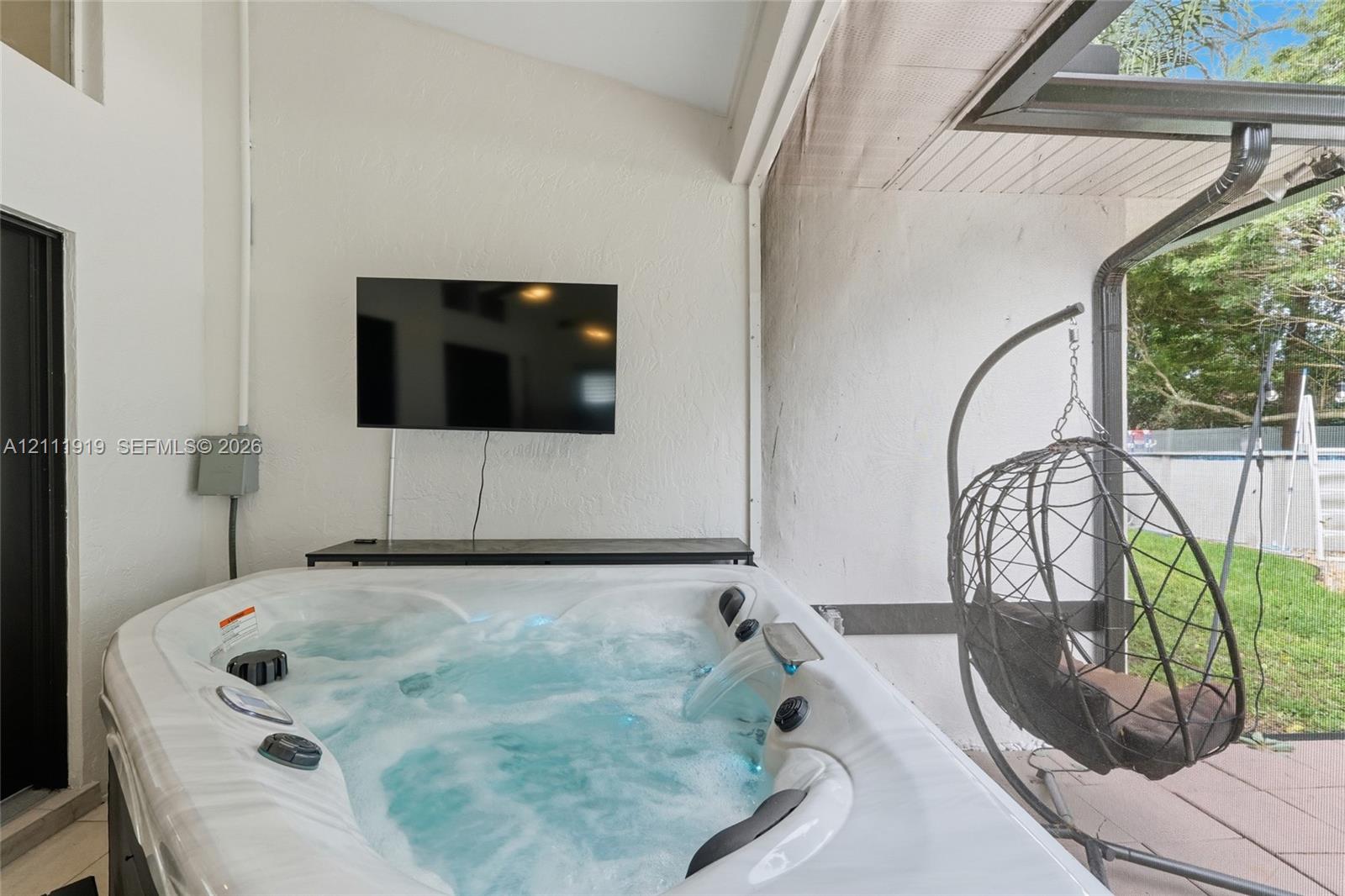 Covered patio featuring an integrated hot tub with water feature, textured exterior walls, and tiled flooring