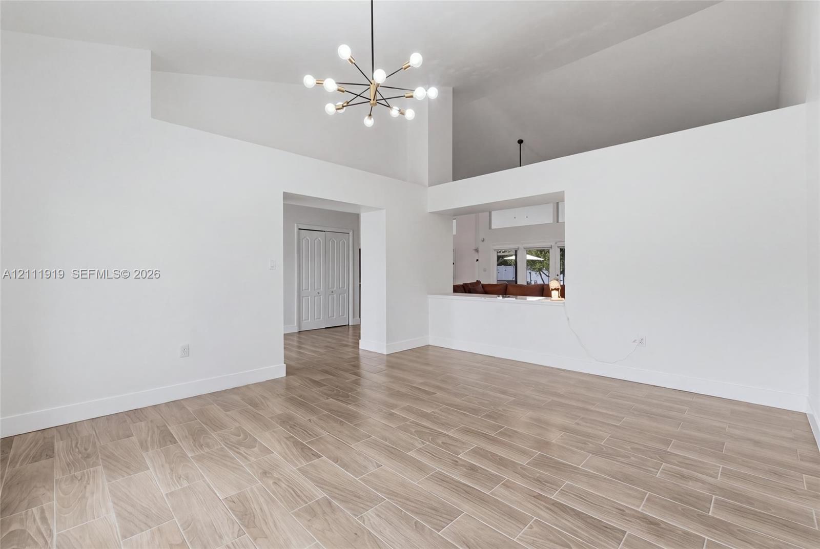 High-volume room featuring a vaulted ceiling, wood-finish flooring, mid-century modern sputnik-style chandelier, and built-in architectural pass-through