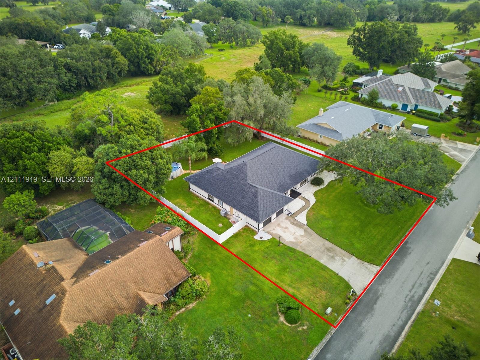 Single-story residence featuring a hipped roof, attached multi-car garage, concrete driveway, and expansive lawn with mature trees Single-story residence featuring a hipped roof, attached multi-car garage, concrete driveway, and expansive lawn with mature trees