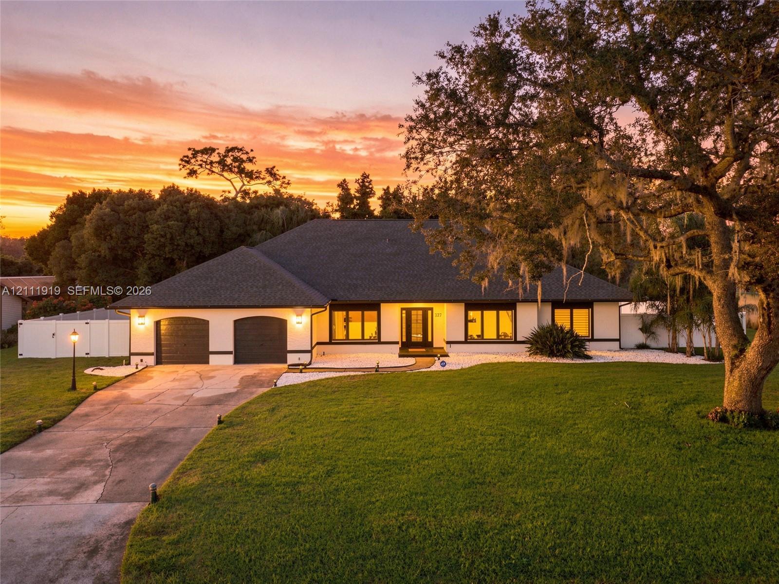 Single-story exterior featuring a hip roof, two-car garage, expansive front lawn, mature oak tree, and stone-accented landscaping Single-story exterior featuring a hip roof, two-car garage, expansive front lawn, mature oak tree, and stone-accented landscaping