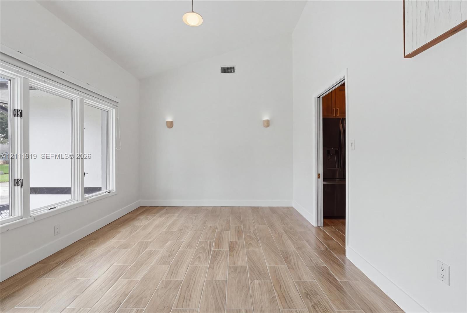 Vaulted ceilings, wood-finish tile flooring, expansive windows, dual wall-mounted light fixtures, and a recessed ceiling light