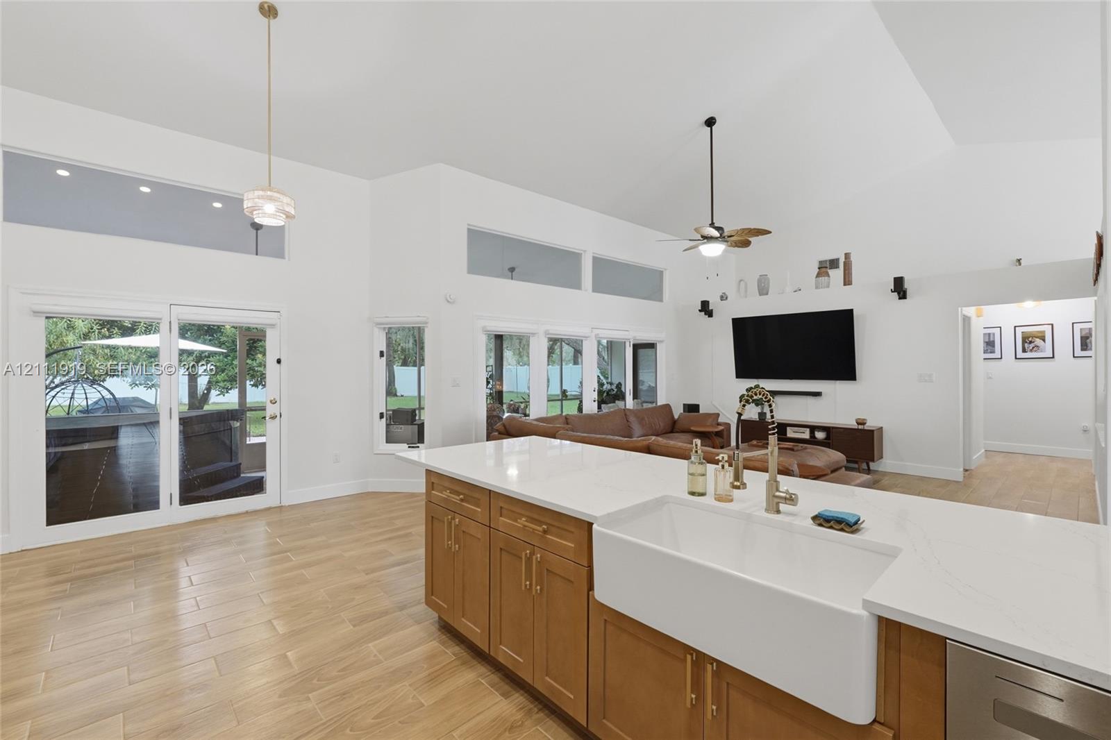 Open floor plan featuring vaulted ceilings, wood-finish flooring, a kitchen island with stone-surface countertop, white farmhouse sink, and transom windows Open floor plan featuring vaulted ceilings, wood-finish flooring, a kitchen island with stone-surface countertop, white farmhouse sink, and transom windows