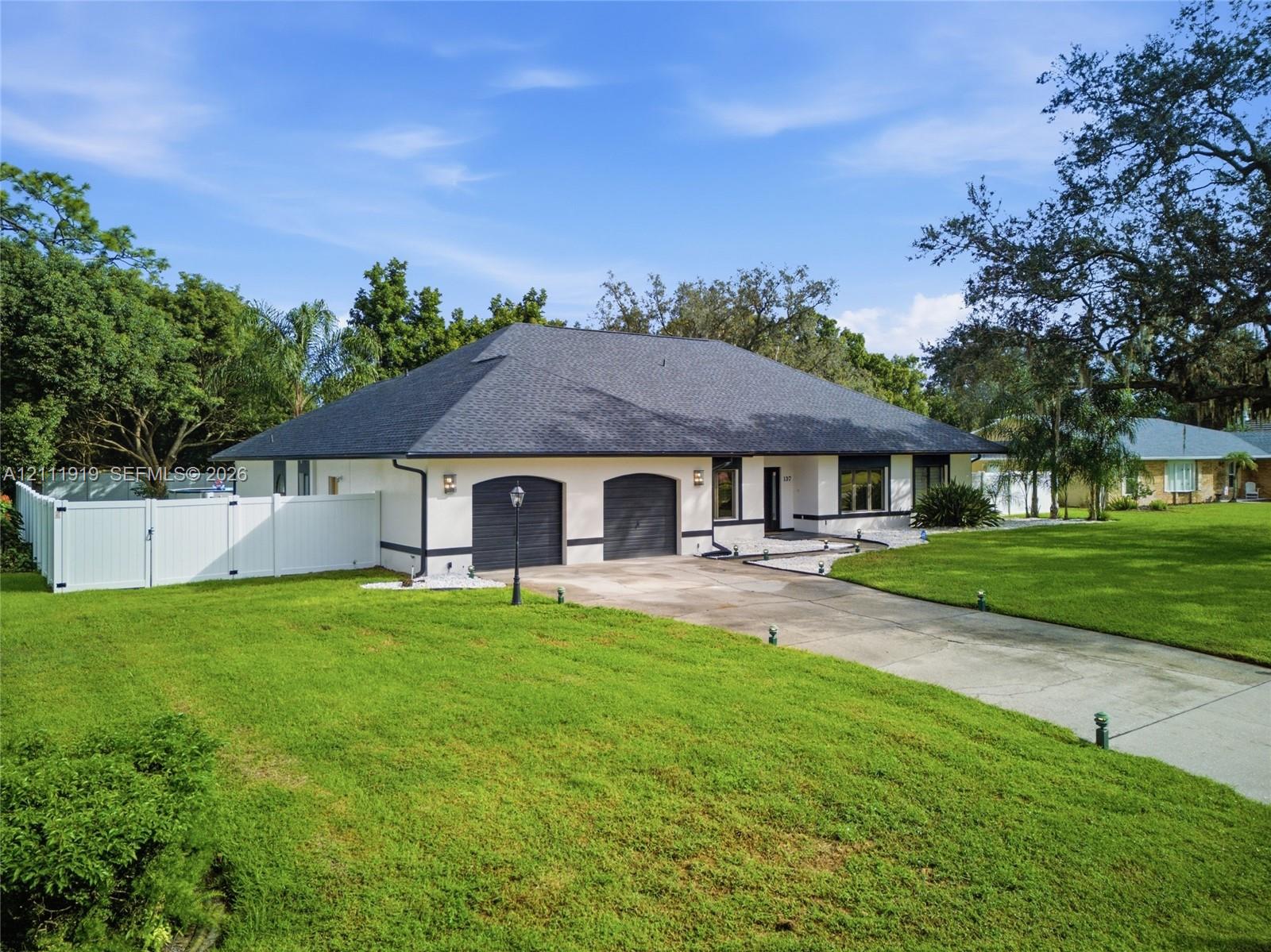 Single-story exterior featuring a light-toned masonry facade, a hipped roof with dark shingles, two arched garage bays, and a surrounding privacy fence