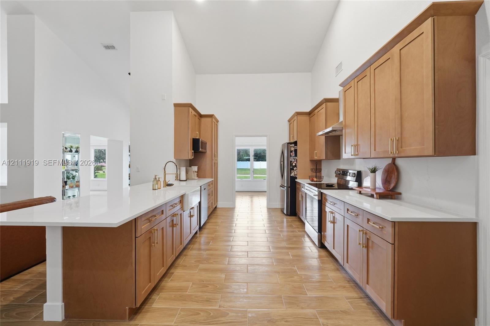 Kitchen featuring vaulted ceilings, light-toned shaker cabinetry, quartz countertops, a farmhouse-style apron sink, and wood-finish tile flooring Kitchen featuring vaulted ceilings, light-toned shaker cabinetry, quartz countertops, a farmhouse-style apron sink, and wood-finish tile flooring