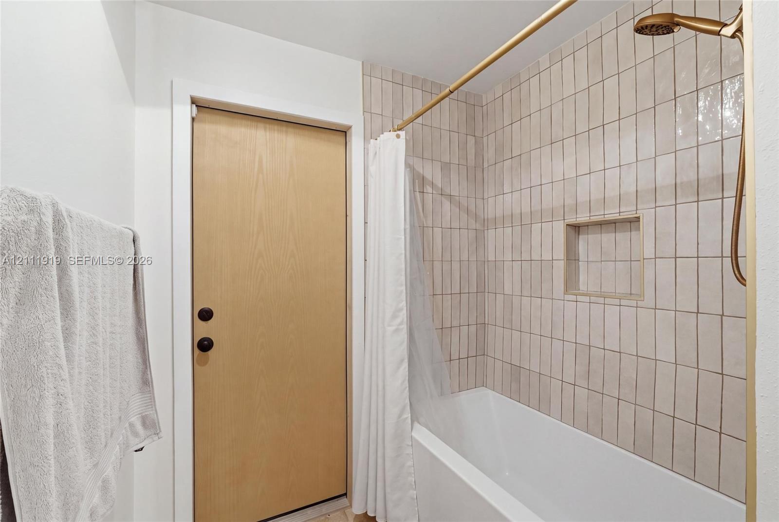 Full bathroom featuring a tub-shower combination with floor-to-ceiling vertical ceramic wall tiles, a built-in recessed wall niche, and metallic hardware finish