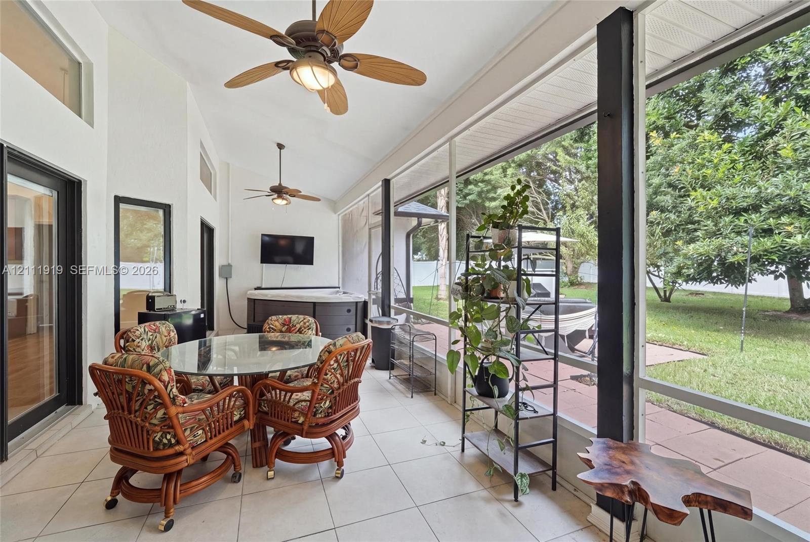 Screened-in porch featuring vaulted ceilings, dual ceiling fans, tile flooring, and integrated wall-mounted exterior light fixtures